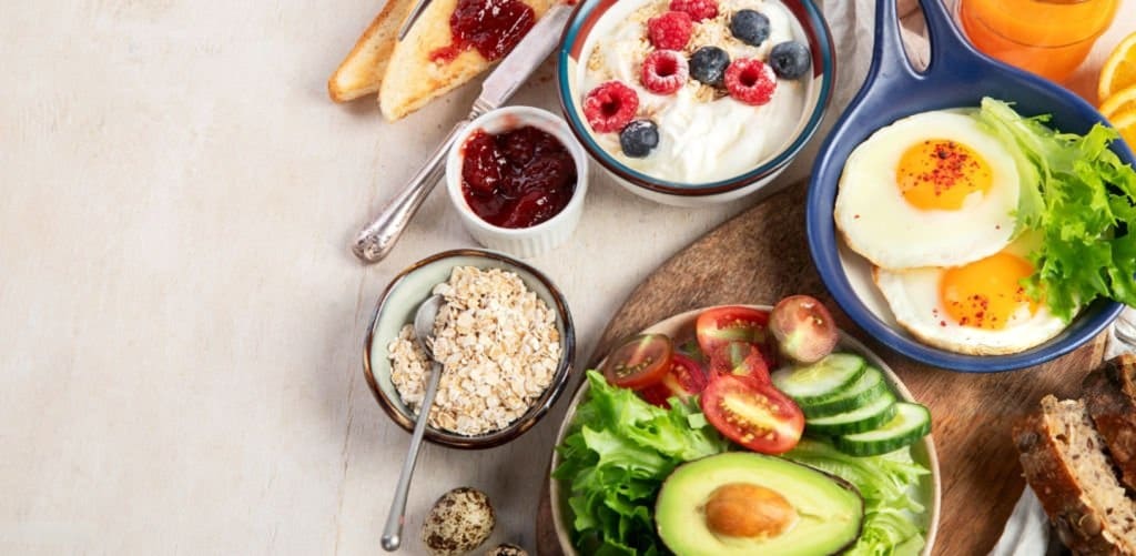 A well-balanced breakfast plate with eggs, avocado toast, and a bowl of oatmeal with berries.